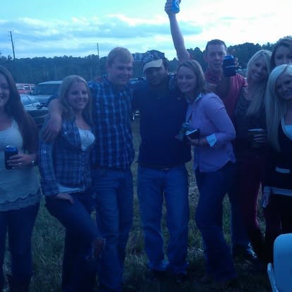 Arms around friends in the field, one hand raised cheering.